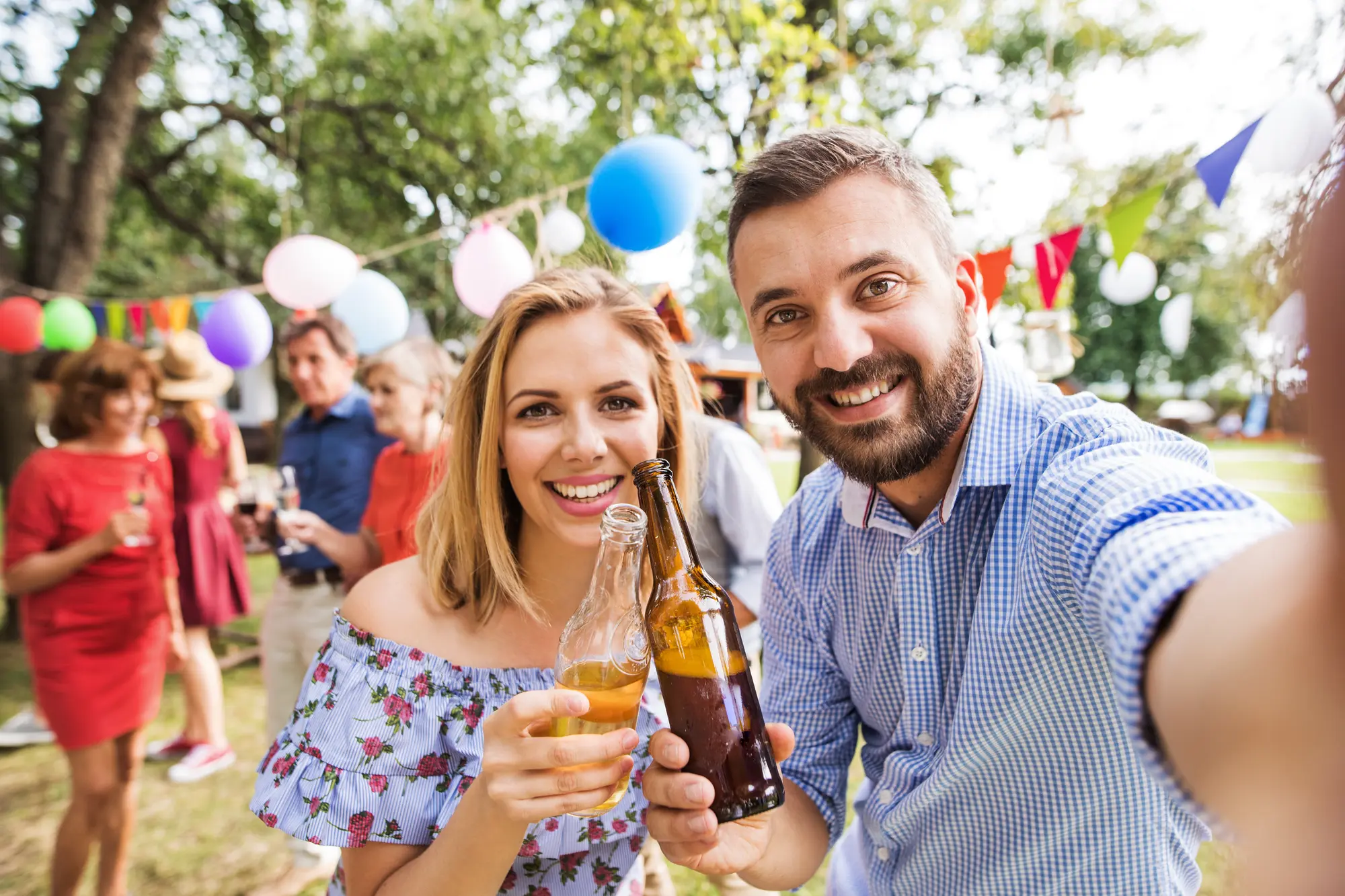 Zwei Gäste stoßen auf einem sommerlichen Gartenfest an und machen ein Selfie