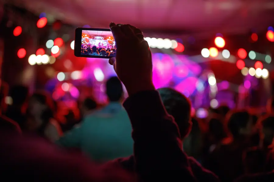 Person filmt eine Bühne bei einer Abendveranstaltung mit dem Smartphone